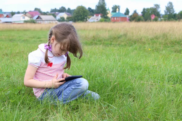 Маленькая девочка сидит и играет с планшетным компьютером на зеленом мясе возле v — стоковое фото