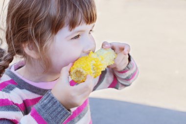 Güzel küçük bir kız haşlanmış mısır yaz açık yiyor