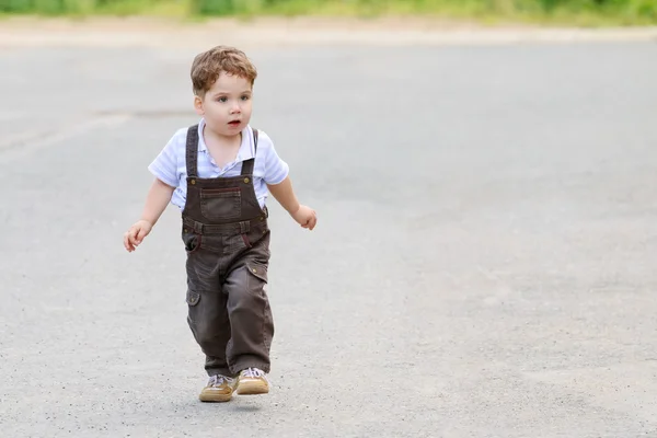 Cute beautiful little boy in brown suit, walks on asphalt road — Stock Photo, Image