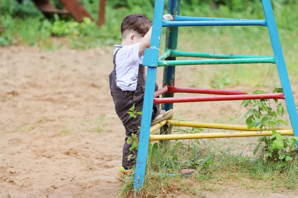 Schattige kleine knappe jongen in bruin pak klimt op speelplaats — Stockfoto