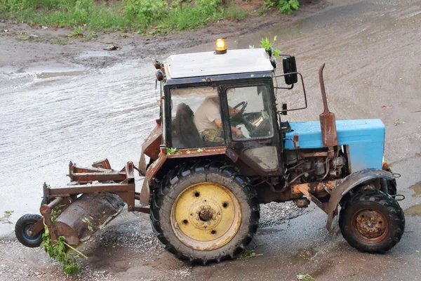 Blue old and rusty tractor running after rain storms and summer