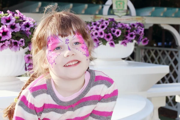 Felice bambina con farfalla viola raffigurata sul viso vicino a po — Foto Stock