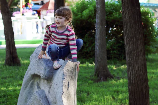 Pretty smiling little girl sits on huge gray stone in summer par — Stock Photo, Image