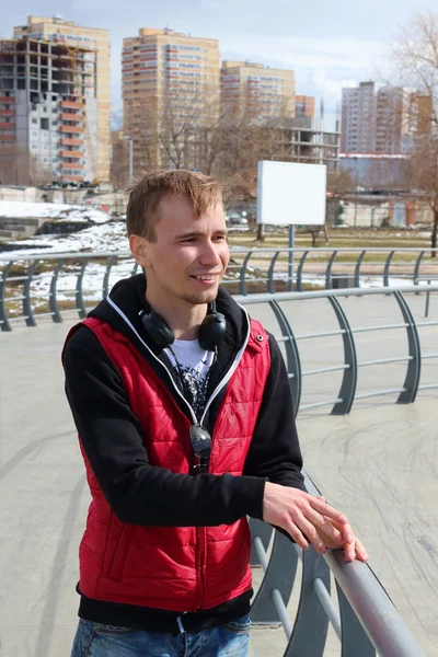 Young man in red vest and with headphones stands on street at sp — Stock Photo, Image