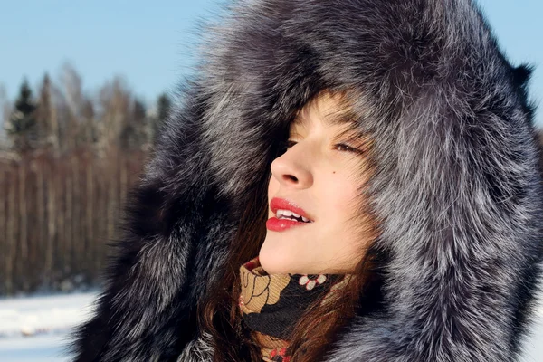 Menina bonita em casaco de pele com capuz olha para o exterior ensolarado — Fotografia de Stock