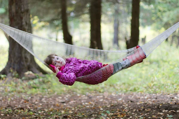 Pequeña chica seria en botas de goma se encuentra en la hamaca en el bosque en autu —  Fotos de Stock