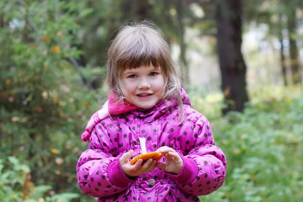 Pequena menina sorridente em rosa segura cogumelo e olha para a acmera a — Fotografia de Stock