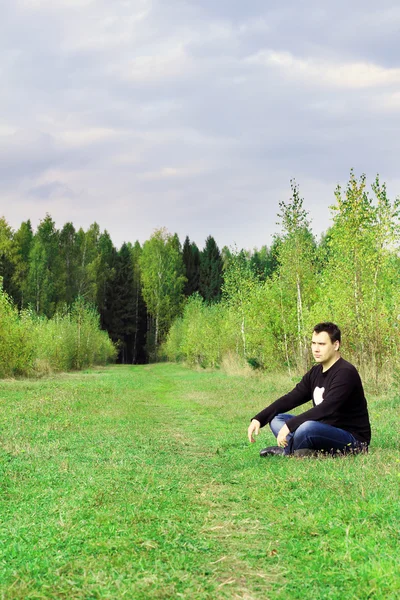 Man sits on grass on edge of forest at autumn dull day and think — Stock Photo, Image