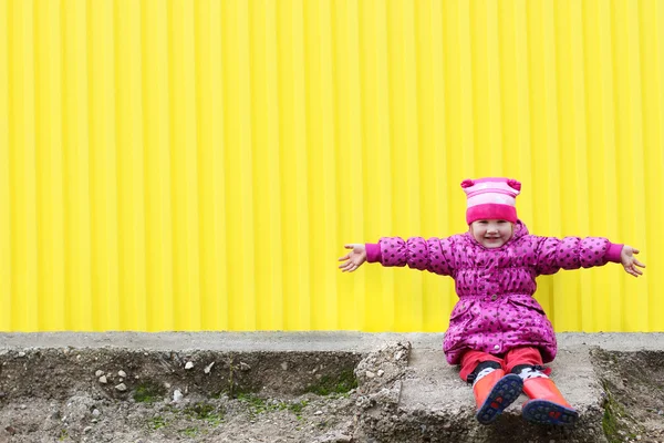 Little pretty girl in gumboots sits near yellow wall with arms o — Stock Photo, Image