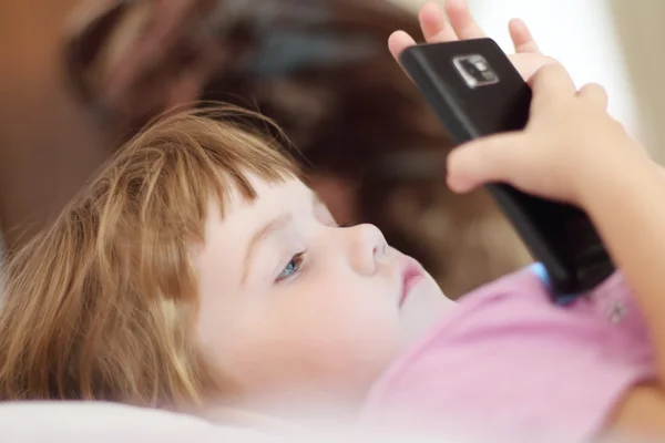 Маленькая серьезная красивая девушка в розовом лежала с телефоном. Шш — стоковое фото