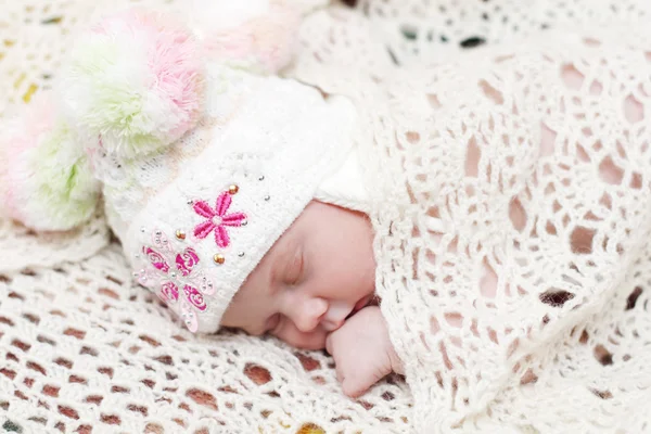 Baby in hat lies on bed under soft white knitted shawl and sleep — Stock Photo, Image