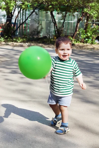 Happy little handsome boy holds green balloon and smiles outdoor — Stock Photo, Image