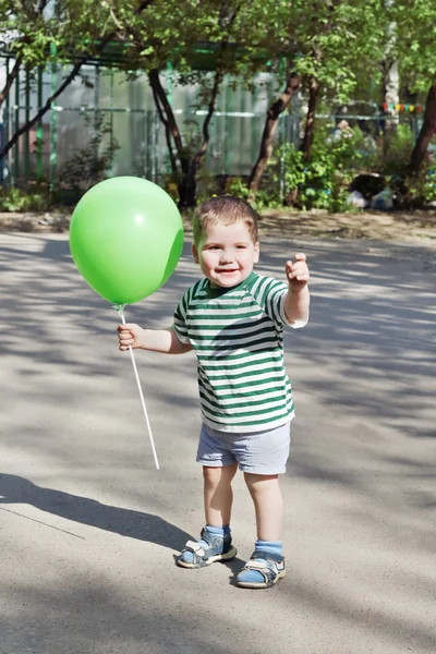 Zadowolony ładny chłopiec trzyma zielonego balonika i uśmiechy odkryty — Zdjęcie stockowe