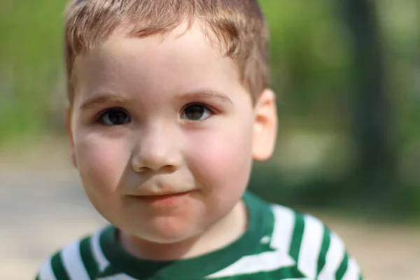 Camera in park kijkt glimlachend weinig schattige jongen. Ondiepe dof — Stockfoto