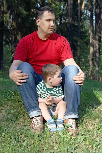 Happy young father with little cute son sit on grass in summer f — Stock Photo, Image