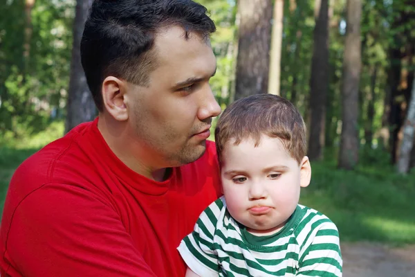 Knappe jonge vader met schattig zoontje zitten in zomer bos — Stockfoto