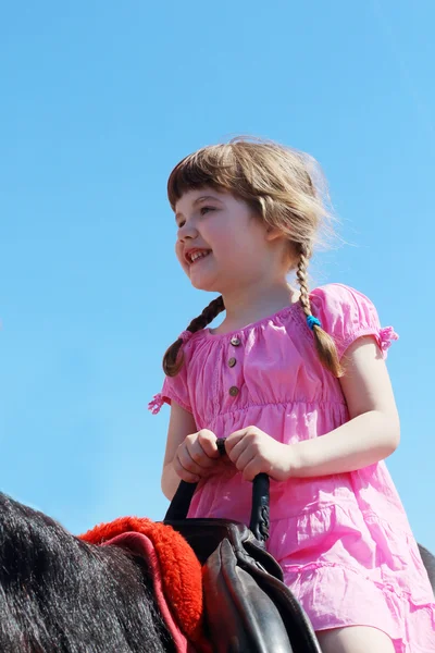 Mooi meisje in roze jurk zit in het zadel op bruin hors — Stockfoto