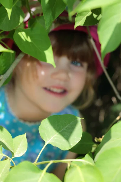 Cute smiling girl in blue dress looking through branches with le — Stock Photo, Image