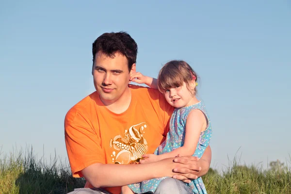 Father and daughter sitting in green meadow in sunny summer day — Stock Photo, Image