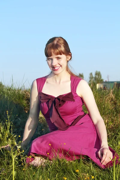 Menina sorridente bonita em vestido rosa sentado na grama em s ensolarado — Fotografia de Stock