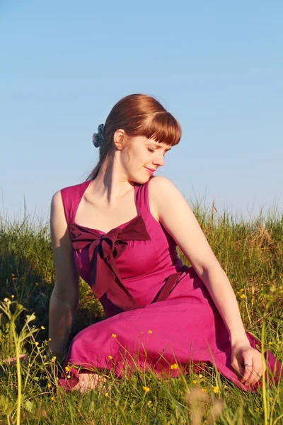 Piękna dziewczyna w różowej sukience siedząc na trawie w słoneczne letnie da — Zdjęcie stockowe