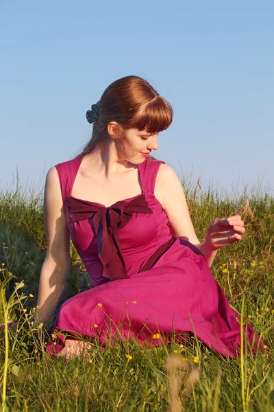 Beautiful girl in pink dress sitting on grass turning her head i — Stock Photo, Image