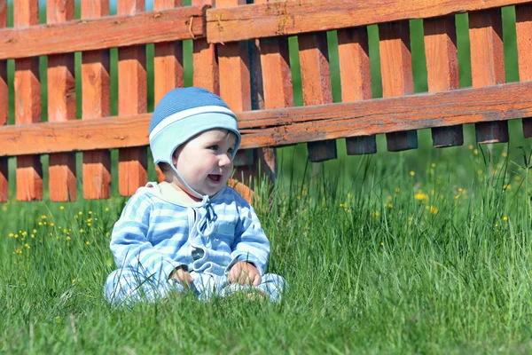 Mavi çizgili takım elbise ve şapka yeşil gr üzerinde oturan küçük şirin çocuk — Stok fotoğraf