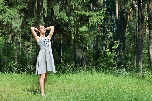 Beautiful girl in dress corrects hair standing on grass on sunny — Stock Photo, Image