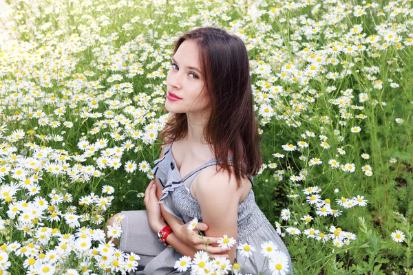 Beautiful girl with clock on hand in dress sits in chamomile flo — Stock Photo, Image