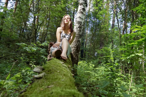 Beautiful girl in dress with long hair sits legs stretched on fa — Stock Photo, Image