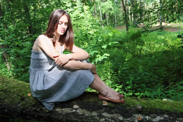 Beautiful girl in dress with long hair sits on fallen tree in fo — Stock Photo, Image