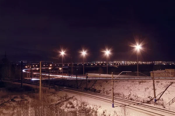 Νυχτερινή άποψη του σιδηροδρόμου με φανάρια και τα φώτα της πόλης στο χειμών — Φωτογραφία Αρχείου