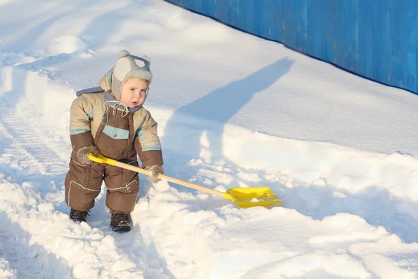 Liten stilig pojke iklädd overall rymmer spade på snö på seger — Stockfoto