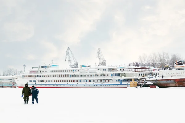 Two fishermen go on ice on frozen river near tourist ship at win — Stock Photo, Image