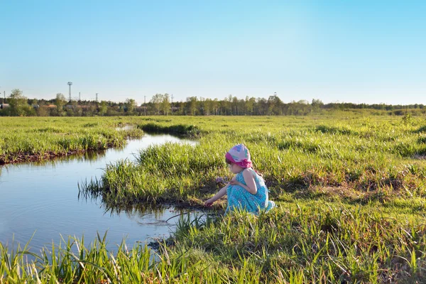 Belle petite fille mignonne en robe bleue assise près du ruisseau avec s — Photo