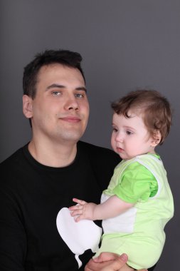 Mutlu yakışıklı baba bebek oğlunun gri studio tutar.