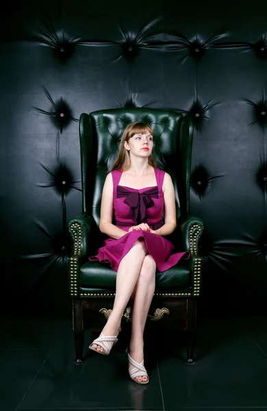 Woman in dress sits in leather armchair in room — Stock Photo, Image