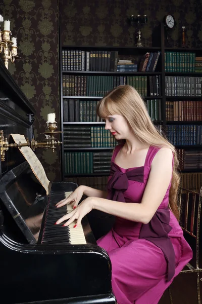 Mujer joven toca el piano en la habitación con estanterías — Foto de Stock