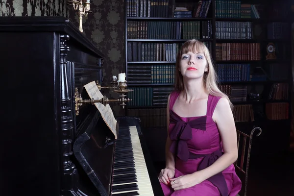 Junge Frau sitzt am Klavier in Raum mit Bücherregalen — Stockfoto