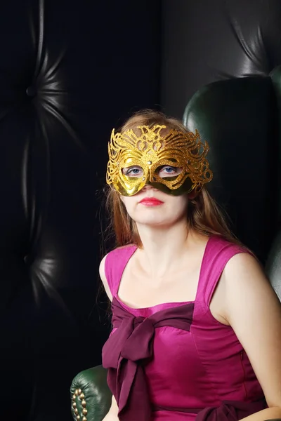 Молодая женщина в позолоченной маске сидит в кожаном кресле в комнате — стоковое фото