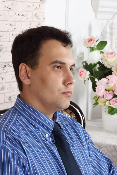 Mooie jonge ernstige man zit in de buurt van tabel met bloemen — Stockfoto