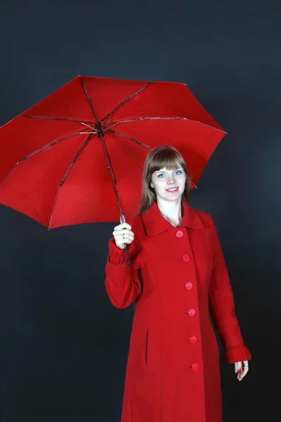 Young woman in red overcoat stands with umbrella and smiles — Stock Photo, Image