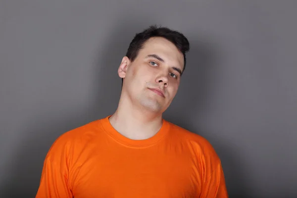 Handsome young man orange t-shirt in grey studio looks at camera — Stock Photo, Image