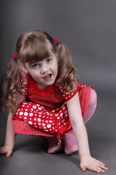 Hermosa niña en vestido rojo se sienta en el suelo en estudio gris —  Fotos de Stock