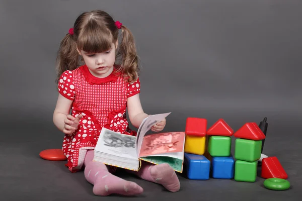 Hermosa niña en vestido rojo se sienta en el suelo y lee libro — Foto de Stock