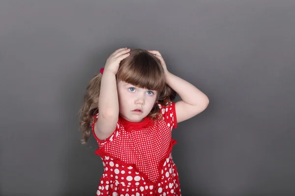 Beautiful little girl in red dress touches her head — Stock Photo, Image