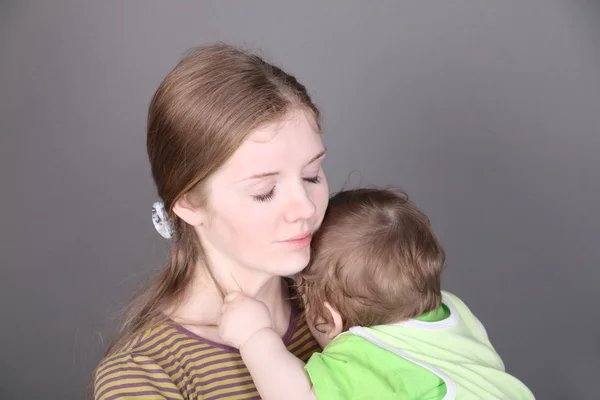 Pretty young mother holds her little baby son in green — Stock Photo, Image