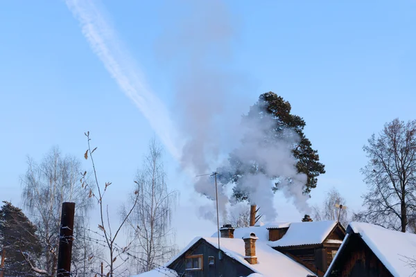 Telhados casas de madeira suburbanas com neve e chaminé com fumaça — Fotografia de Stock