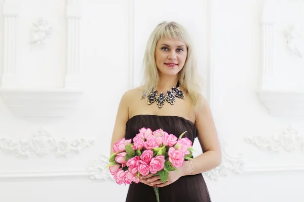 Beautiful woman in brown dress holds pink flowers and sniffs it — Stock Photo, Image