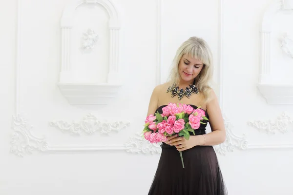 Young pretty woman in brown dress holds pink flowers in white st — Stock Photo, Image